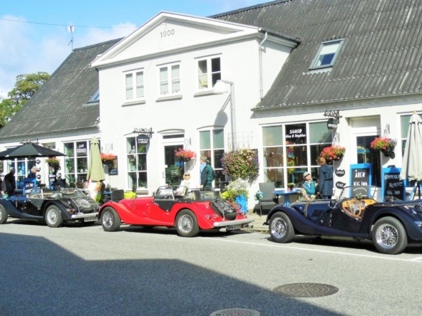 Facade af Café Kunst i Samsø med klassiske biler foran på en solrig dag